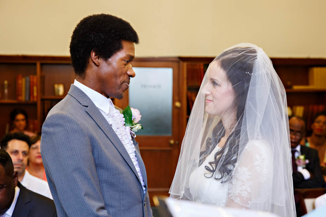 A bride and groom gaze into each others' eyes as they exchange wedding vows. The bride is still wearing her veil.