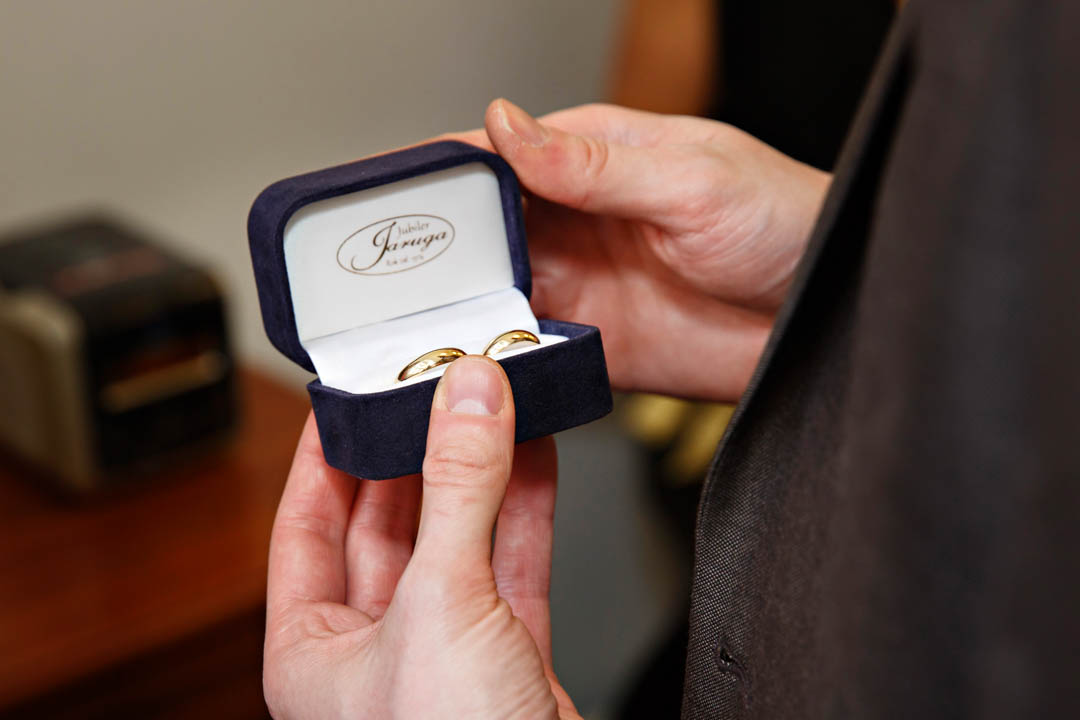A very close up detail photo of the best man holding the open ring box, containing two matching gold wedding bands.