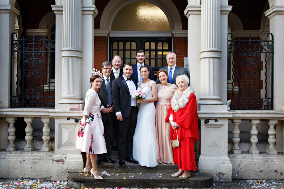 A small family group gathers for a formal wedding photo on the steps of Mayfair Library.