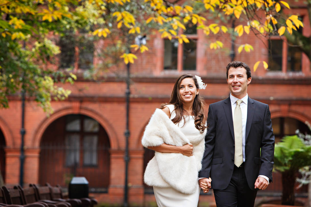 A bride and groom stroll hand in hand through the autumnal park after getting married in the Marylebone Room at Mayfair Library.