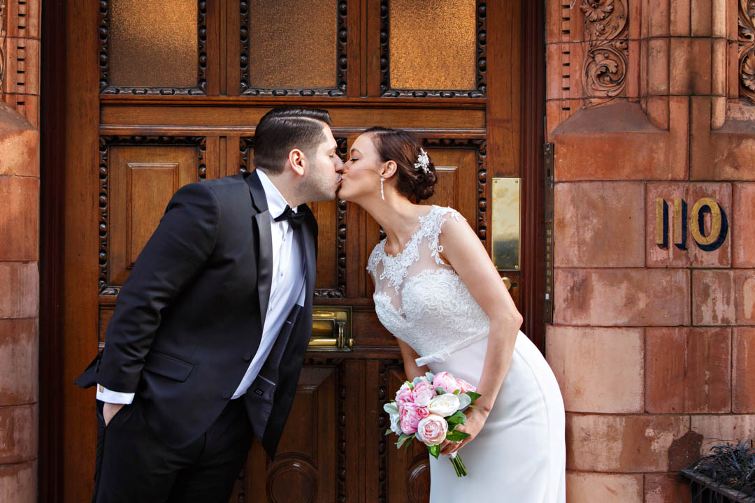 A cute shot of a bride and groom causally leaning in for a quick peck on the lips across a backdrop of a beautifully carved door in Mayfair.