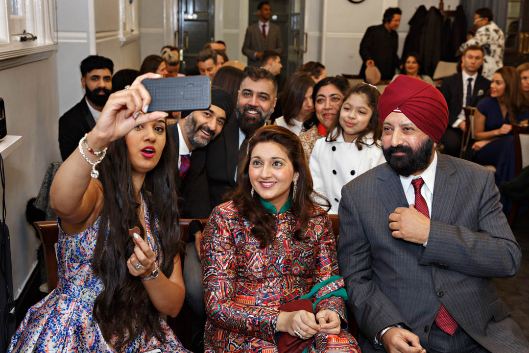 Sikh wedding guests take selfies as they wait for the winter wedding ceremony to begin in the Mayfair Room at Mayfair Library.