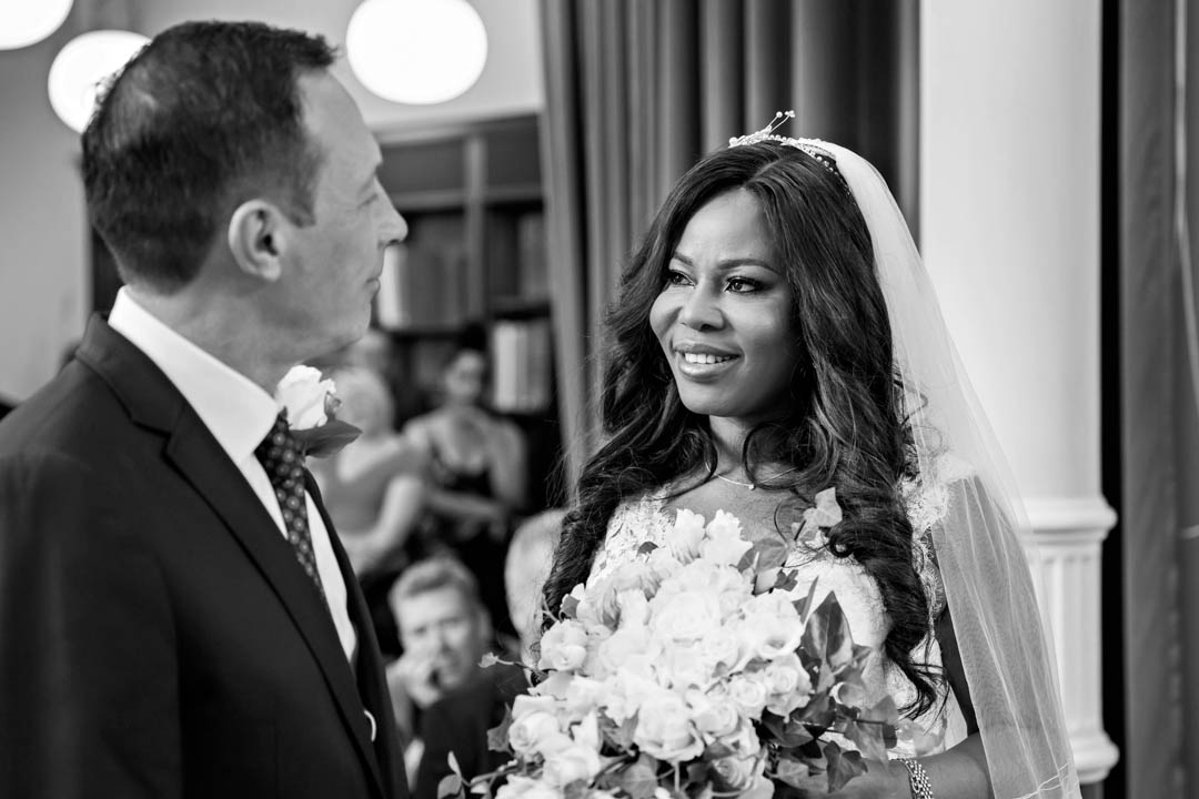 An African bride looks lovingly at her groom as the couple exchange their wedding vows during their Westminster register office wedding ceremony.