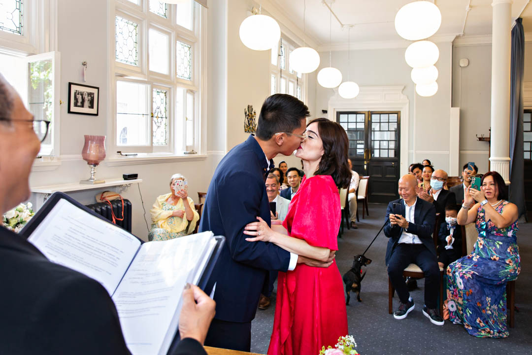 A groom kisses his bride in front of the whole wedding party in the Mayfair Room at Mayfair Library to celebrate that they are now husband and wife.