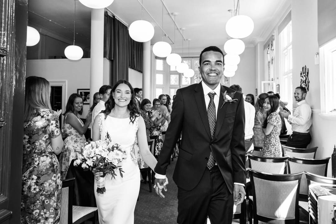 A black and white photograph of a very happy bride and groom exiting the Mayfair Room at Mayfair Library as husband and wife.