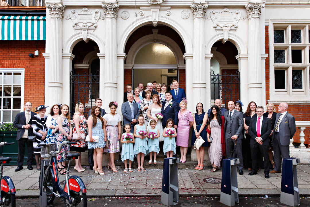 A large wedding group formally arranged to ensure that every guest can be seen clearly on the steps of Mayfair Library. You can see rental bicycles in front of the wedding party as there is a bike docking station right in front of the library, and it cannot be guaranteed that there won't be bikes parked there.